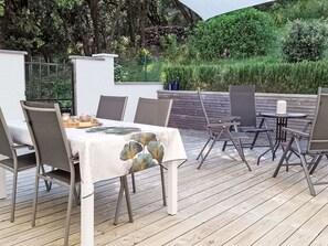 An outdoor dining area with a table set for four, surrounded by chairs, on a wooden deck. - Lucinkas Ferienhaus mit 2 Schlafzimmern by Interhome (La Tour sur Orb)