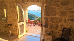 Una habitación con paredes de piedra y un arco abierto que da a un espacio al aire libre con una mesa y sillas.