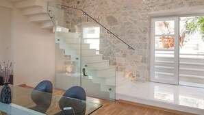 Un interior moderno con una escalera de cristal, una zona de comedor con mesa de cristal y una pared de piedra.