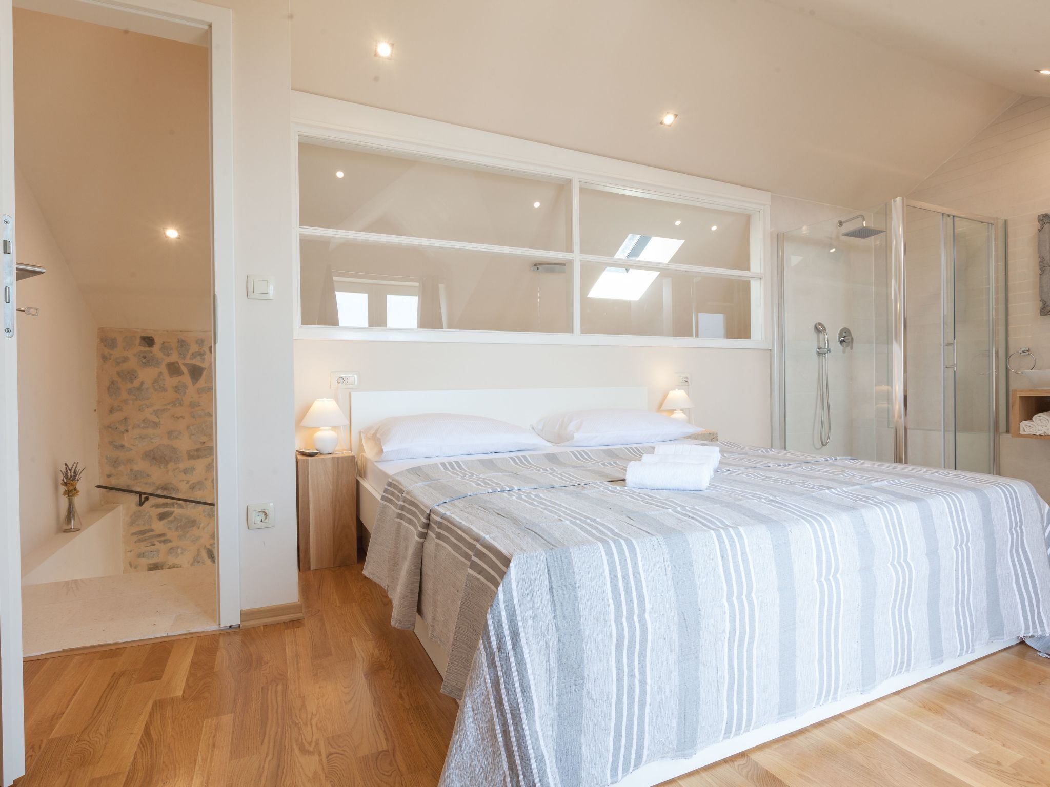 A bedroom with a large bed, a shower area, and a stone wall.