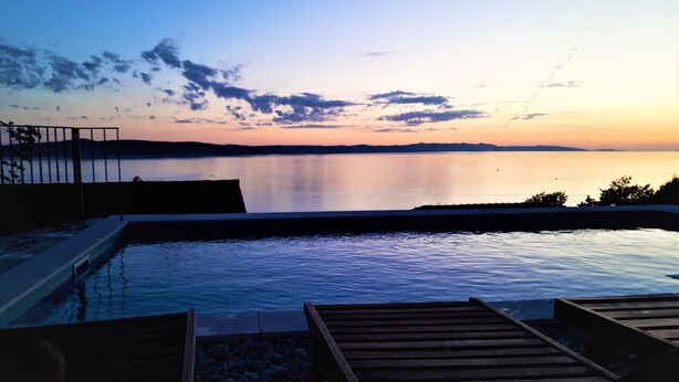 Una piscina con tumbonas de madera y vista a un lago tranquilo al atardecer.