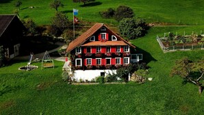 A large, two-story house with a red roof and white walls, surrounded by a lush green field and a small garden. - Oberwilen by Interhome (Vitznau)