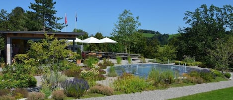 A modern building with a covered outdoor seating area, a small pool, and a well-maintained garden.
