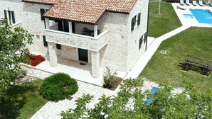 Una casa de piedra de dos pisos, con techo de tejas, piscina y césped bien cuidado.