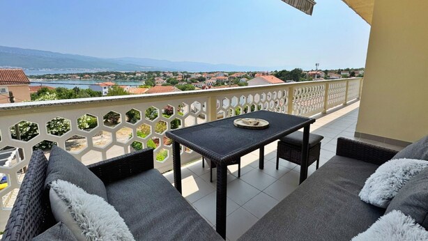 Ein Balkon mit Tisch und zwei Sofas, der einen herrlichen Blick auf einen See und ferne Berge bietet.