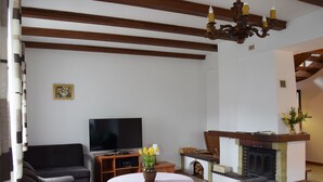Ein Wohnzimmer mit einer Couch, einem Fernseher, einem Kamin und einer Chandelier.