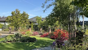 Een tuin met een geplaveid pad, diverse bloeiende planten en een bakstenen muur.