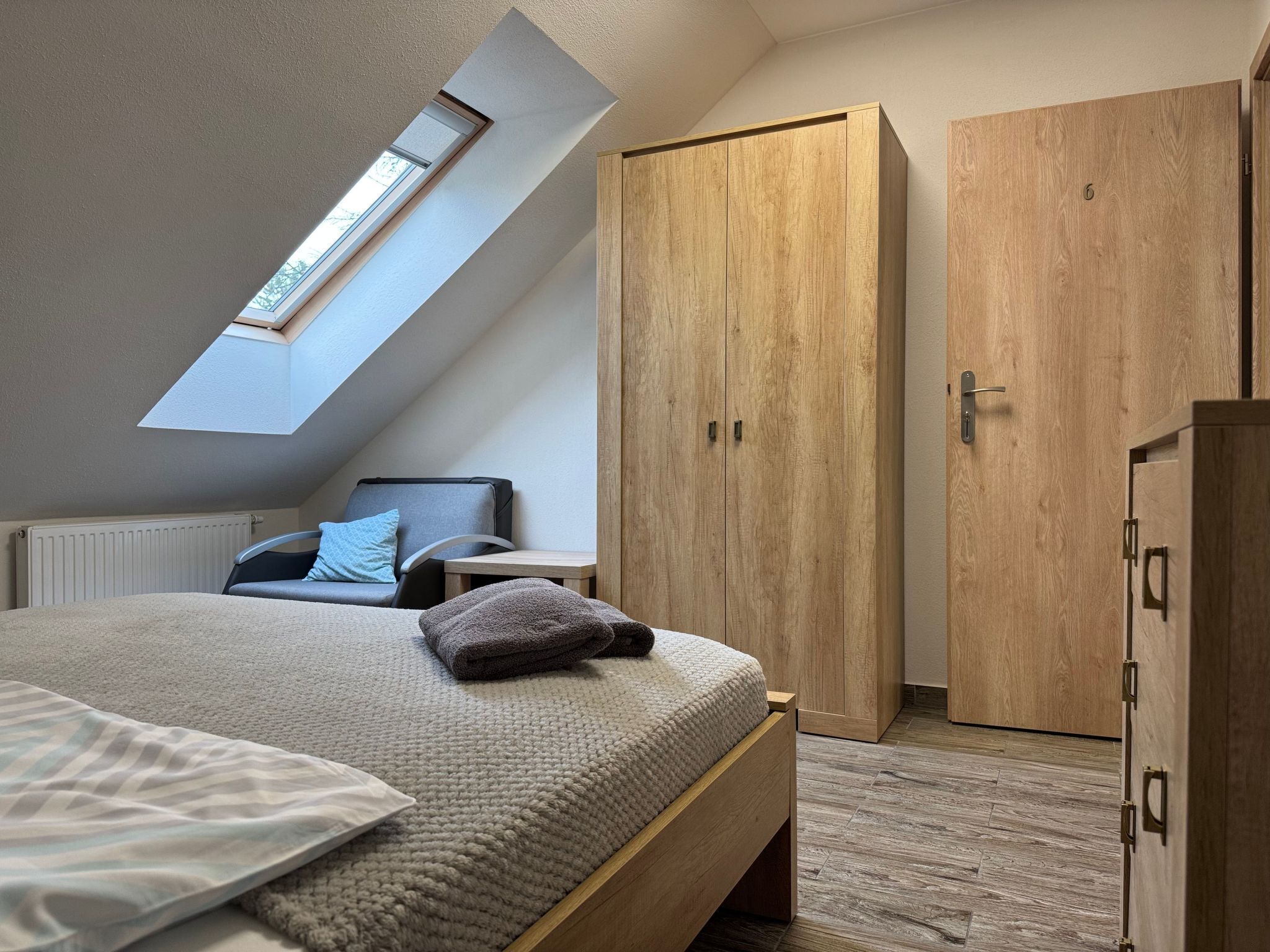 Une chambre avec un plafond en pente, un puits de lumière, un lit, une armoire et une table de chevet.