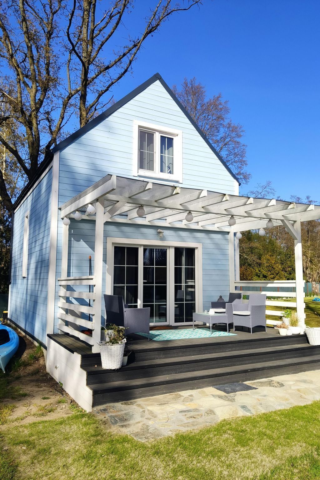 Ein Haus mit überdachter Terrasse, Sitzgelegenheiten im Freien und einem kleinen Garten.