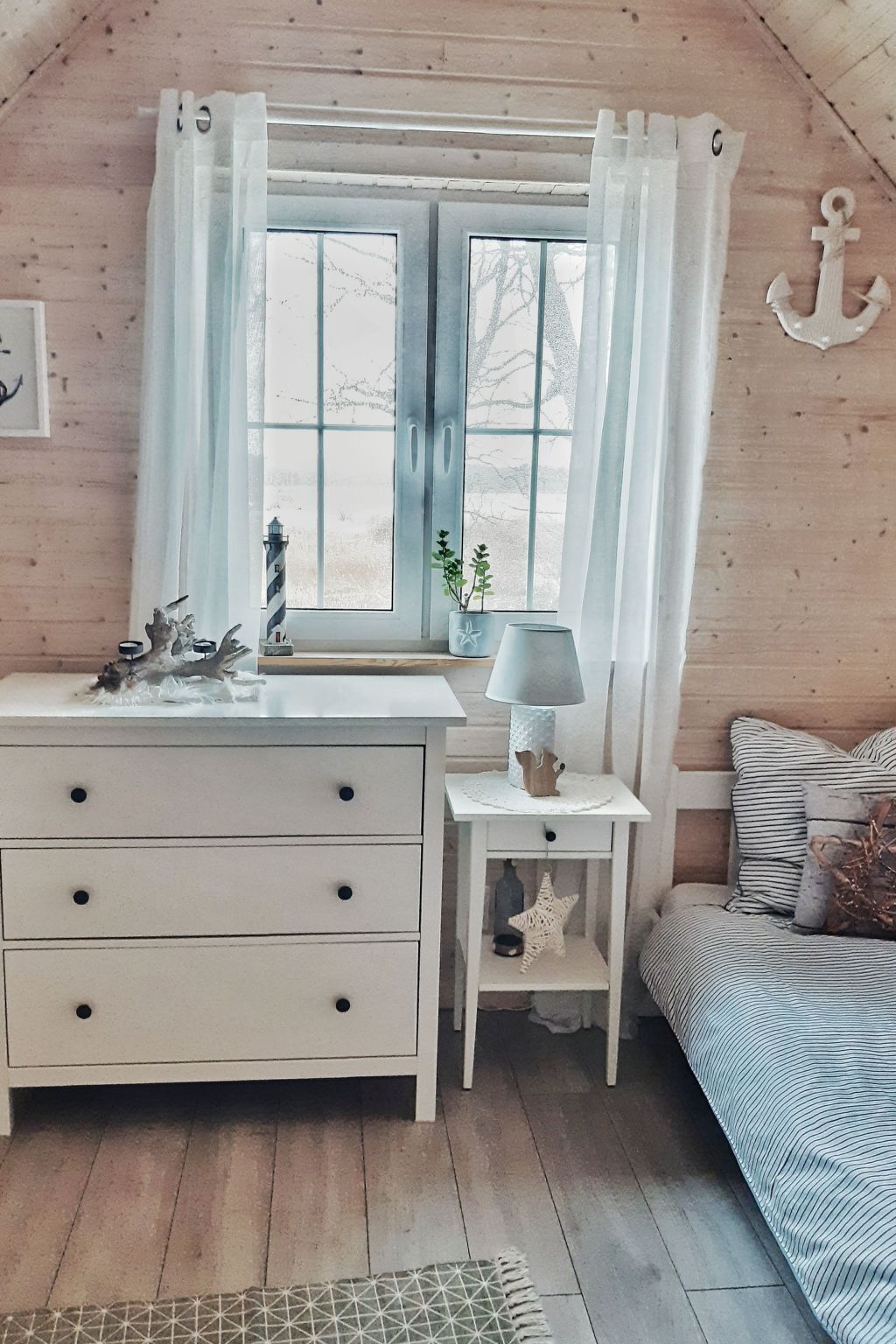 Une chambre confortable, aménagée dans le style d’un chalet, avec un intérieur en bois, un lit avec une literie à rayures, une table de chevet avec une lampe et une fenêtre avec des rideaux.