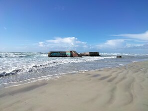 Ein sandiger Strand mit brechenden Wellen und großen Betonkonstruktionen mit Graffiti im Wasser.