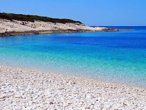 Ein Kiesstrand mit klarem, blauem Wasser und einer felsigen Küste.