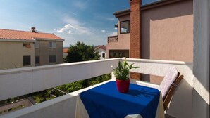 Ein Balkon mit blauem Tischläufer, einem roten Blumentopf und einem weißen Stuhl.