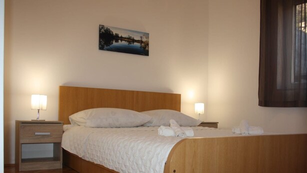 Ein ordentlich bezogenes Bett mit einem hölzernen Kopfteil, zwei Nachttischen mit Lampen und einem Bild an der Wand.