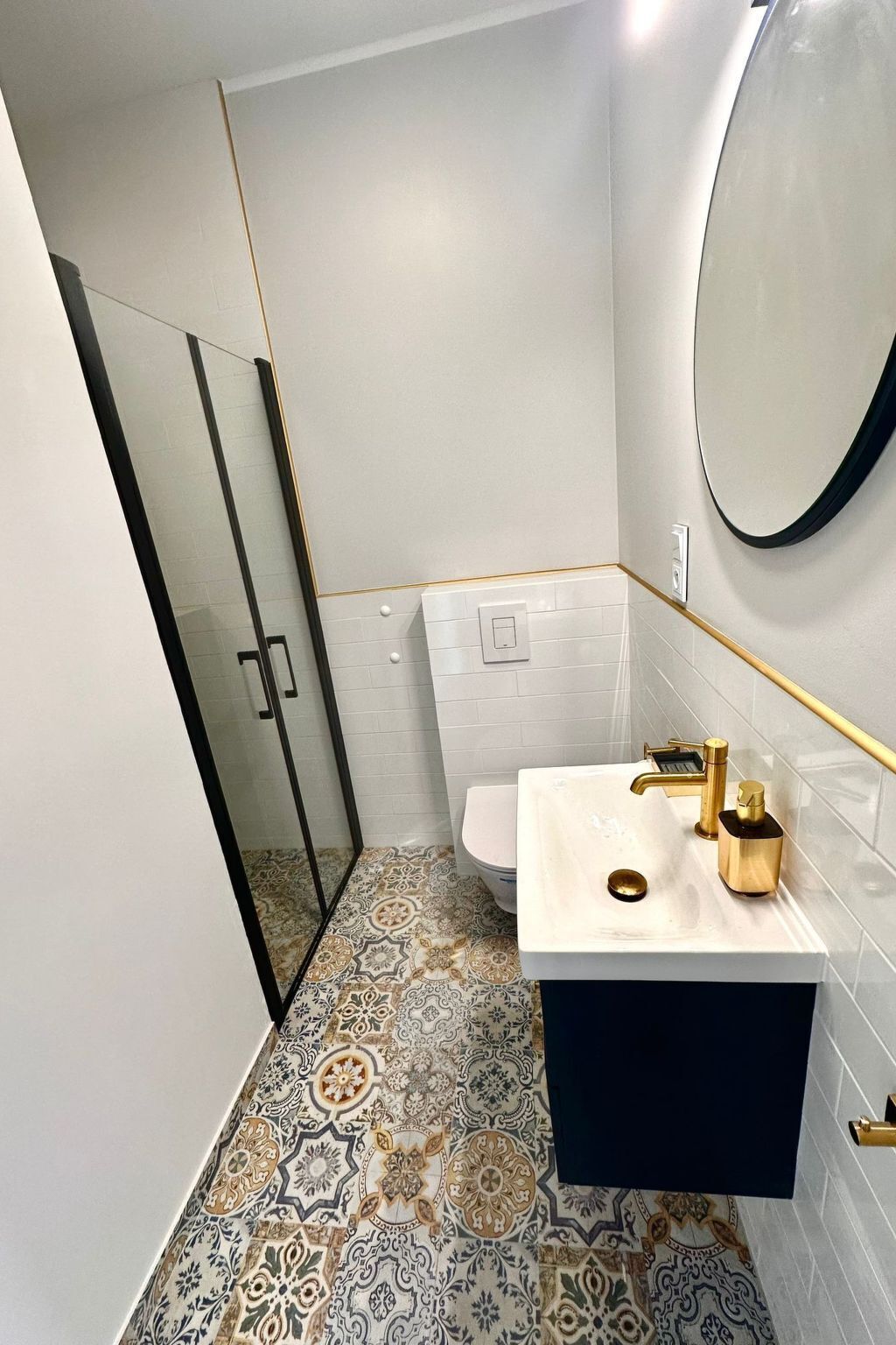 Une salle de bain moderne avec un carrelage décoratif, un lavabo blanc doté de robinetterie dorée et une douche à parois en verre.