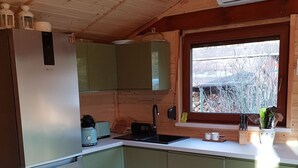 Eine kleine Küche mit grünen Schränken, einem Holztisch und einem Fenster mit Blick auf Bäume.
