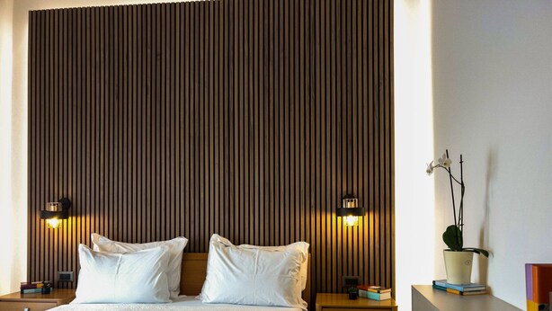 Habitación de hotel con una cama grande, dos mesitas de noche, una lámpara de noche, una pequeña planta en maceta y una estantería.