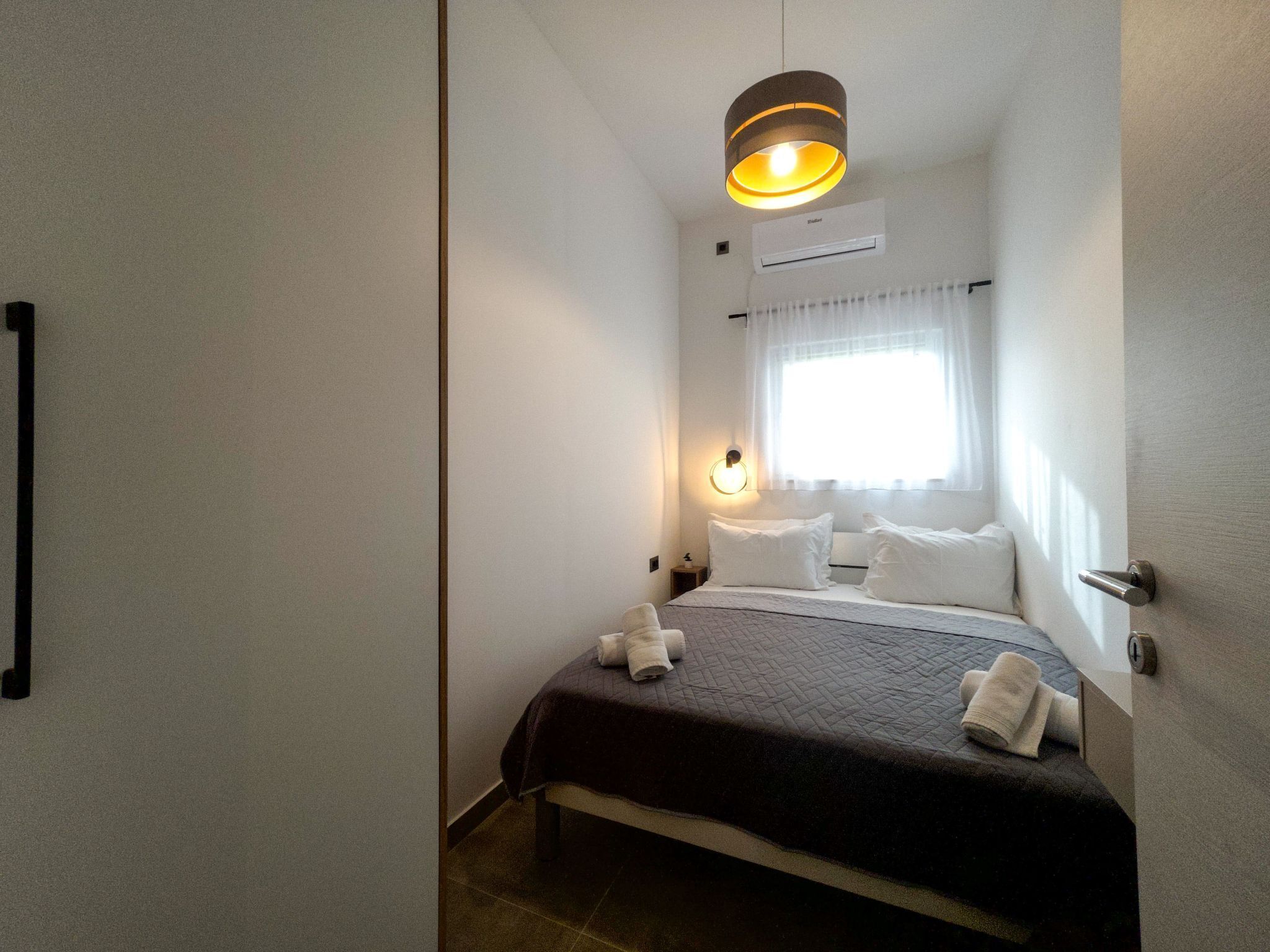 A bedroom with a bed, a bedside table, a lamp, and a window with curtains.