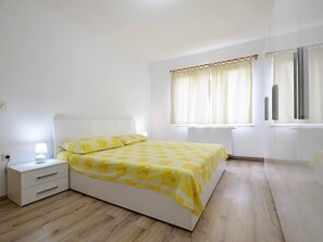 A bedroom with a bed, bedside table, lamp, window with curtains, and a radiator. - Wohnung Goranka 1 by Interhome (Dragišina)