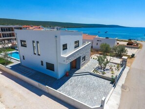 Um edifício moderno de dois andares com piscina, situado perto de uma área costeira com barcos na água.