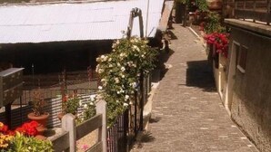 A narrow stone pathway with a wooden fence on one side and a building with a sloped roof on the other. - Chalet Angelika by Interhome (Albinen)