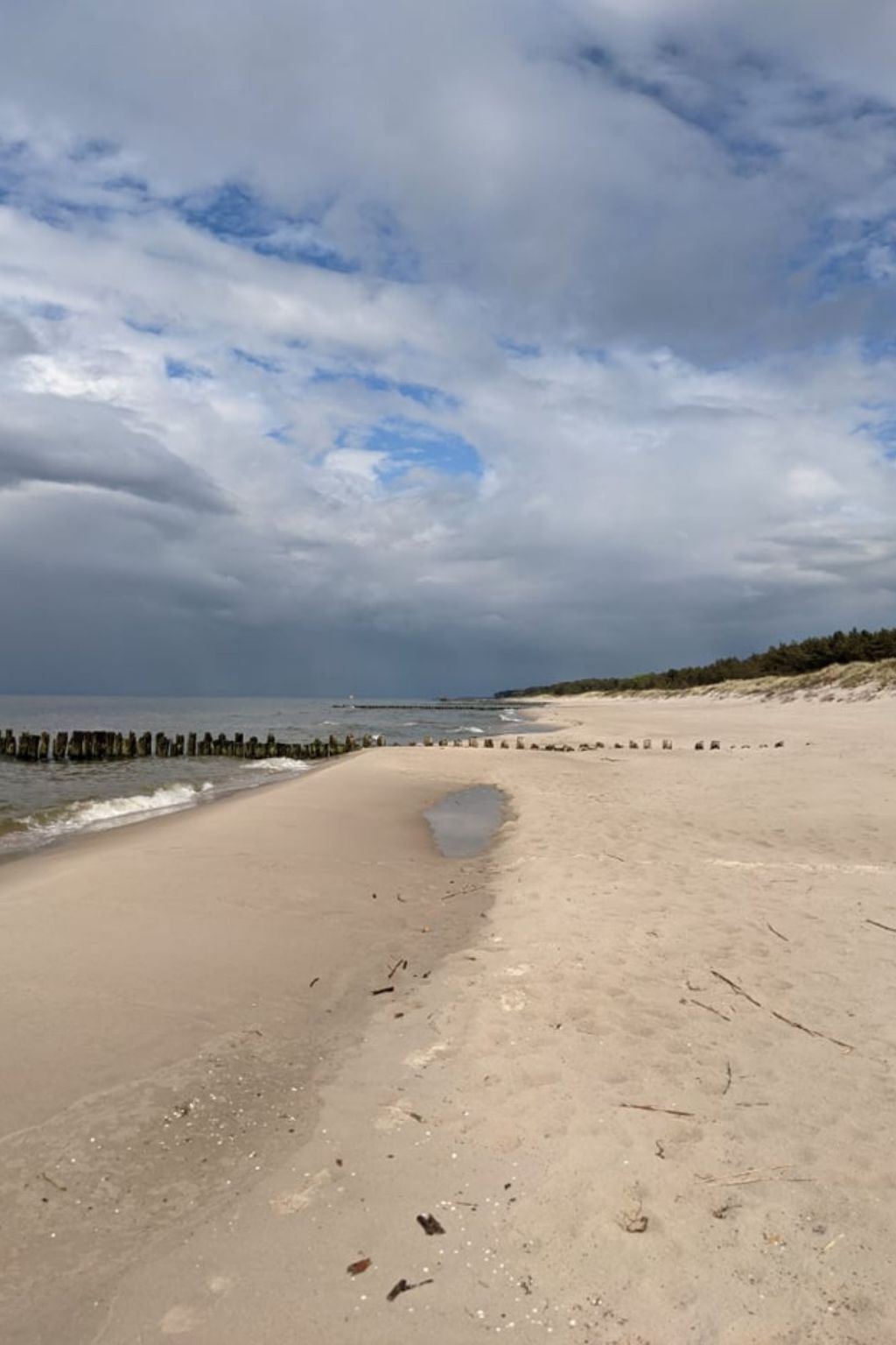 A beach with a wooden jetty, sandy shore, and a cloudy sky.