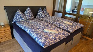 A double bed with a patterned bedspread and matching pillows, a bedside table with a lamp, and a wooden nightstand. - Haus Ahorni by Interhome (Beatenberg)