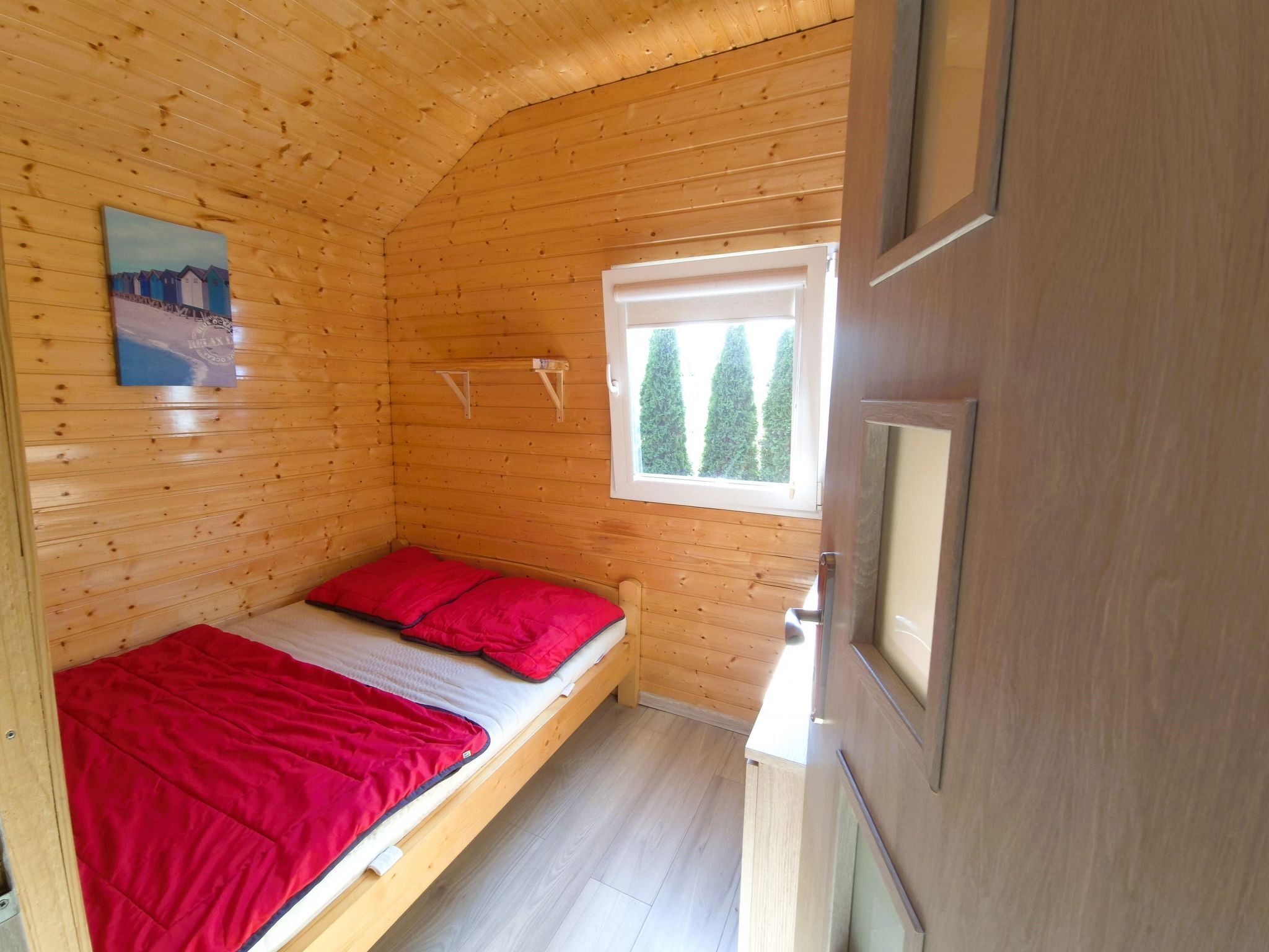 Una habitación de cabaña de madera con una cama, una ventana con vista a los árboles y un cuadro en la pared.