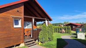 Una baita di legno con veranda, una finestra e un piccolo spazio salotto all'aperto.