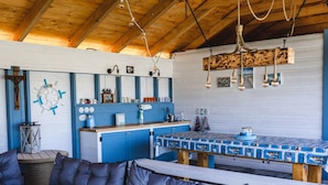 Un accogliente interno di una baita con soffitto in legno, un tavolo da pranzo con tovaglia a tema nautico e un bancone cucina blu.