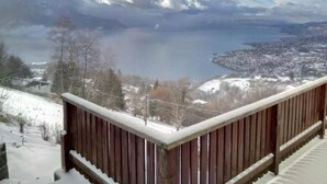 A snowy landscape with a wooden balcony overlooking a lake and a town. - Gais Alpins by Interhome (Montreux)