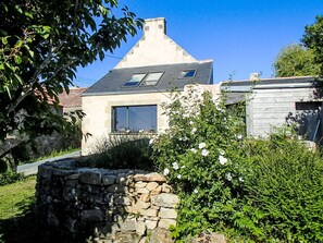 Een huis met een stenen muur, een tuin met witte bloemen en een heldere blauwe lucht.