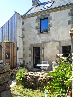 Ein Steinhaus mit einer Holztür, einem kleinen Fenster und einer Terrasse mit Tisch und Stühlen.