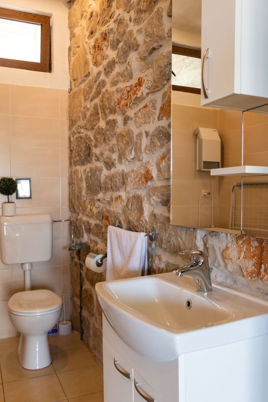 Un baño con pared de piedra, inodoro, lavabo y espejo.