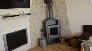 A living room with a stone wall, a fireplace, a TV mounted on the wall, and a sofa. - Panoramablick in Königstein by Interhome (Königstein)