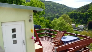 A deck with a wooden bench and a table, overlooking a green landscape with trees and a house in the distance. - Panoramablick in Königstein by Interhome (Königstein)