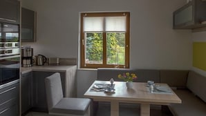 A compact kitchen with a dining area, a window with blinds, and a built-in TV. - Appartement mit Bergblick by Interhome (Bad Elster)