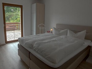 Un dormitorio con una cama grande, un armario y un balcón con terraza de madera.