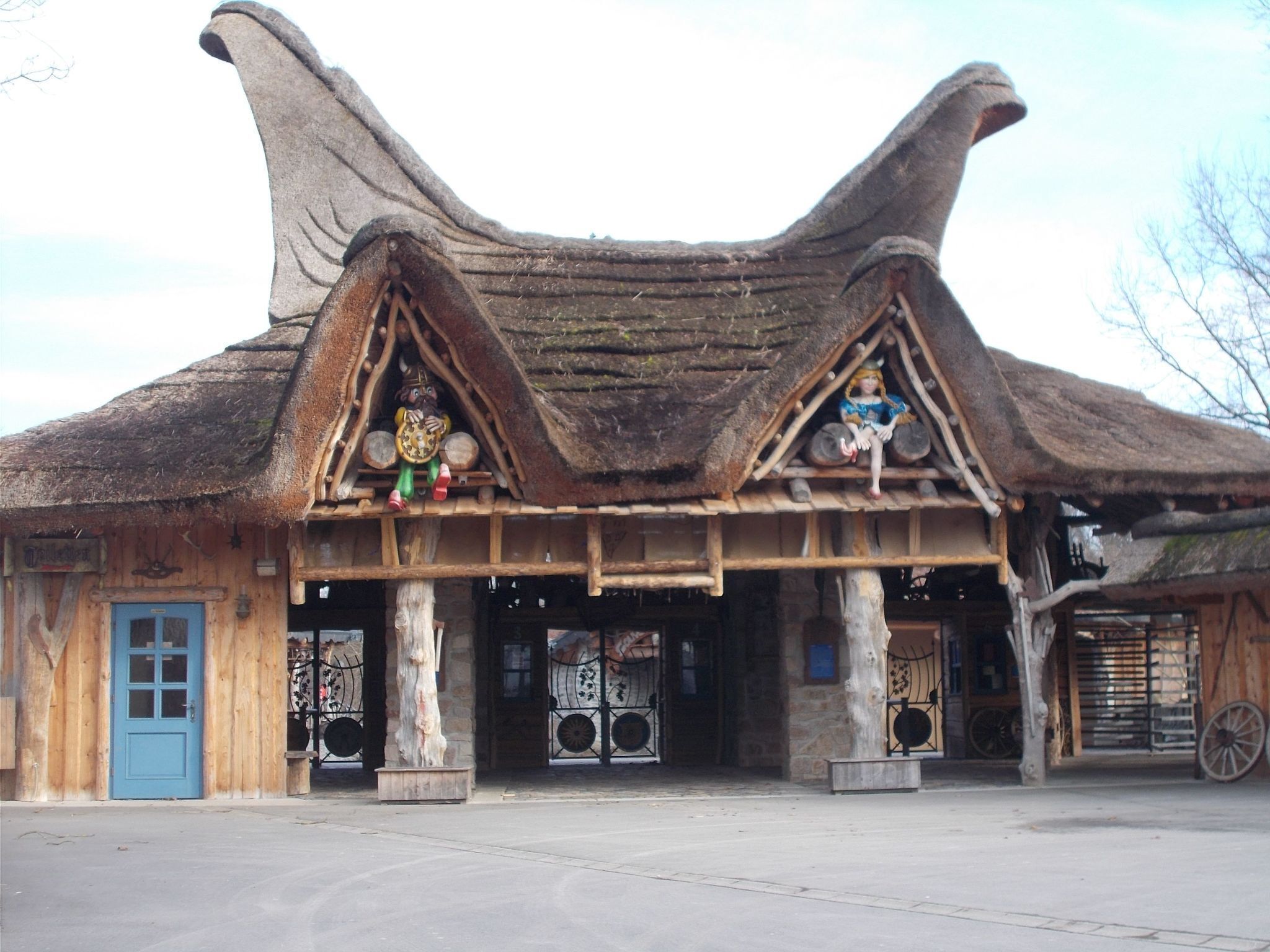A rustic building with a steeply pitched roof, wooden beams, and a blue door.