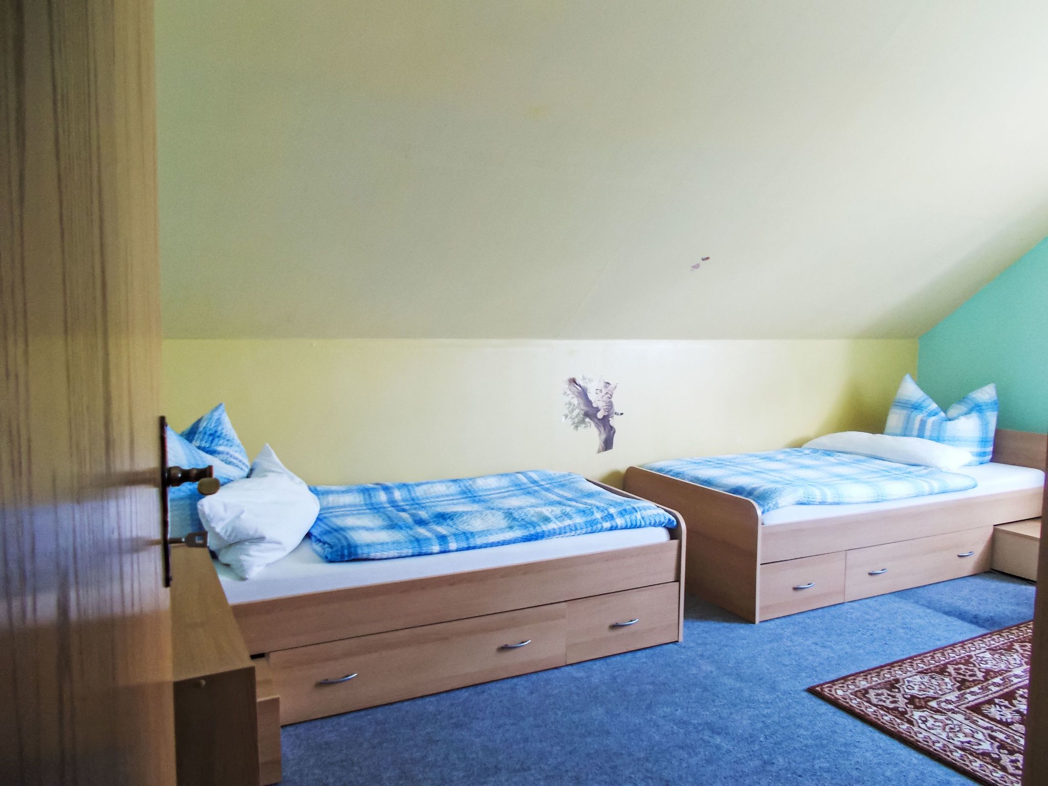 Une chambre à coucher avec deux lits simples, chacun recouvert d’une couverture à carreaux bleus et blancs, dotée de têtes de lit en bois et agrémentée d’une petite décoration murale.