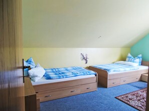 Une chambre à coucher avec deux lits simples, chacun recouvert d’une couverture à carreaux bleus et blancs, dotée de têtes de lit en bois et agrémentée d’une petite décoration murale.