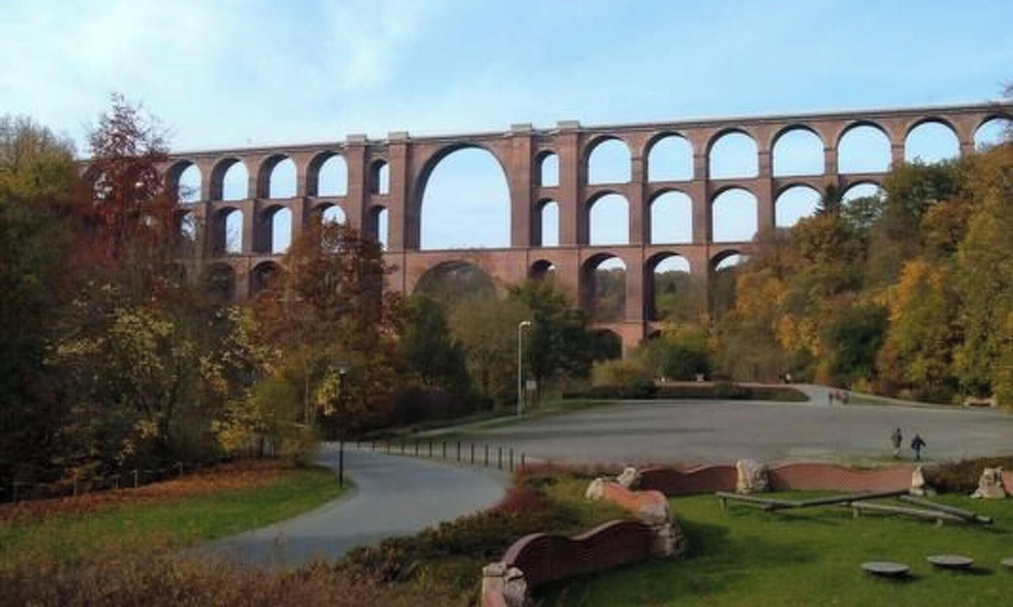 A large stone bridge with multiple arches, surrounded by trees and a pathway.