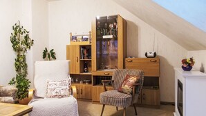 Ein gemütliches Wohnzimmer mit hoher Decke, einem Bücherregal aus Holz, einem gemusterten Sessel und einem kleinen Tisch.