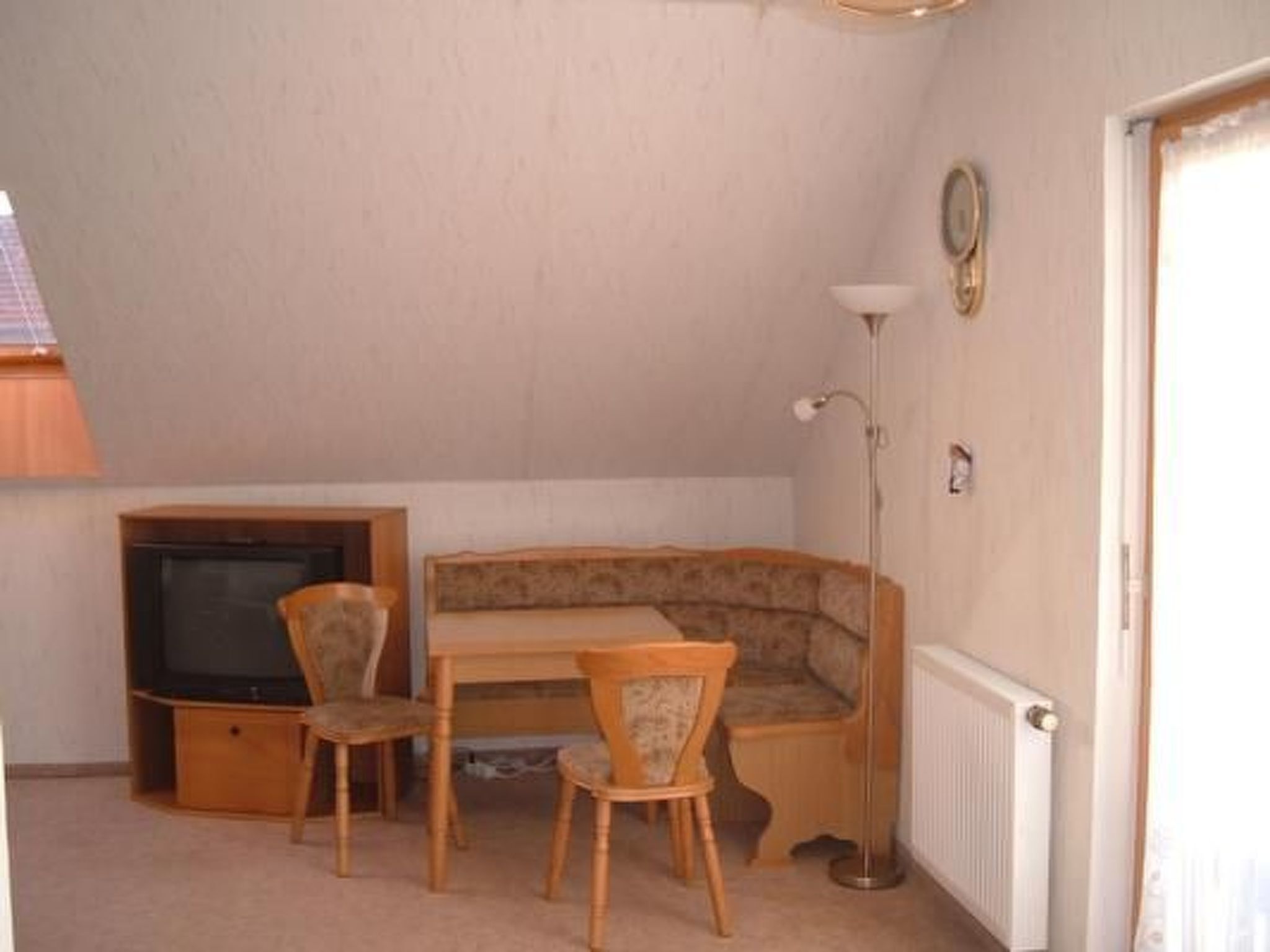 Een kleine, gezellige kamer met een houten tafel en twee stoelen, een televisie en een radiator.