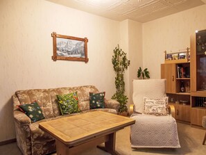 Ein Wohnzimmer mit Sofa, Sessel, Couchtisch, Bücherregal und einem gerahmten Bild an der Wand.