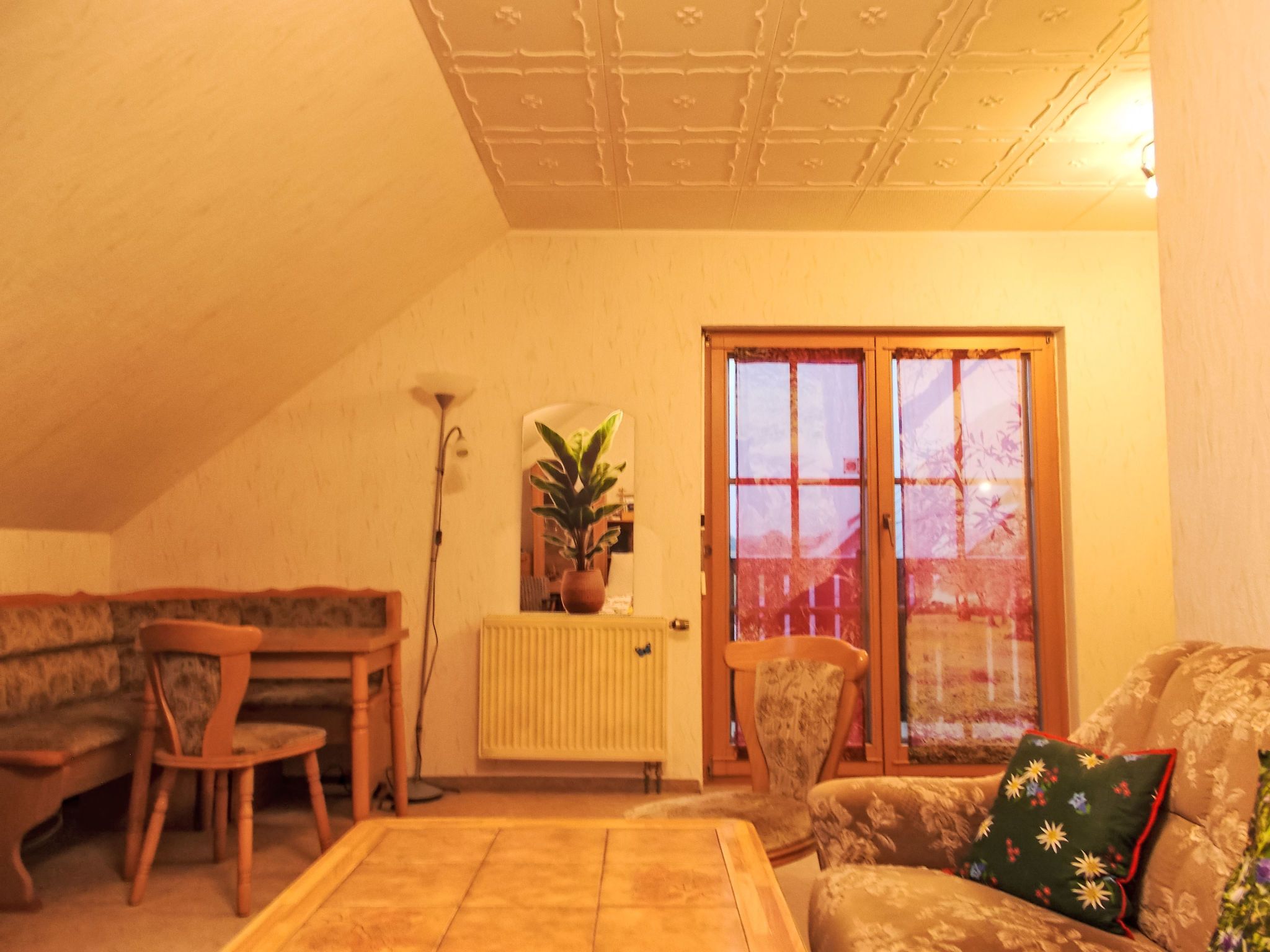 En hyggelig stue med højt til loftet, en radiator, en plante og en skydedør.