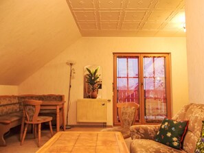 Un salon chaleureux avec un plafond haut, un radiateur, une plante et une porte-fenêtre coulissante.