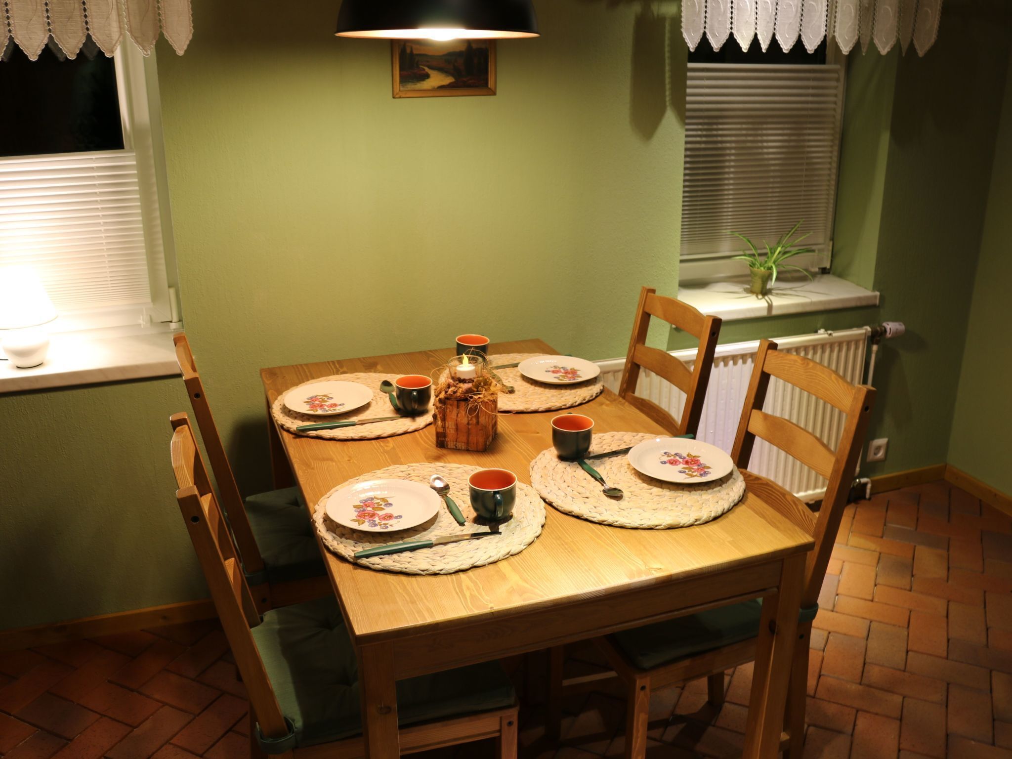 Mesa de comedor preparada para seis personas, con individuales, platos, tazas y un centro de mesa con velas.