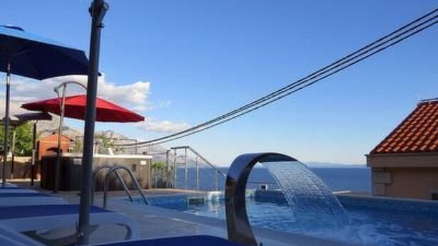 Ett poolområde med solstolar och parasoller, en fontän eller liknande vattendekoration och utsikt över havet.