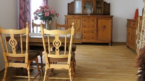 Un coin repas avec des chaises et une table en bois, un buffet en bois doté de portes en verre, et un vase rempli de fleurs.